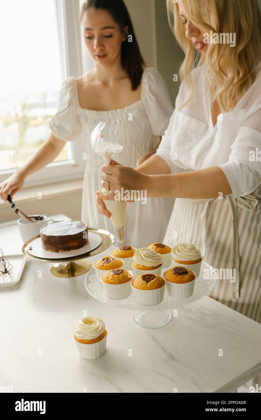 Eine Frau mit einer Freundin, die zu Hause Kuchen zubereitet und Cupcakes dekoriert Stockfoto