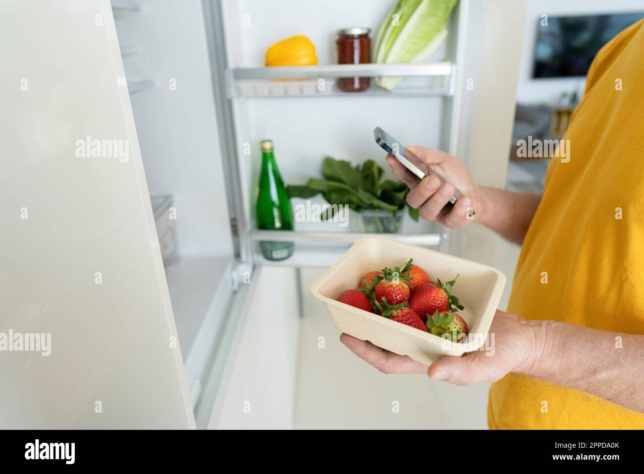 Senior-Mann mit frischen Erdbeeren und Smartphone zu Hause Stockfoto