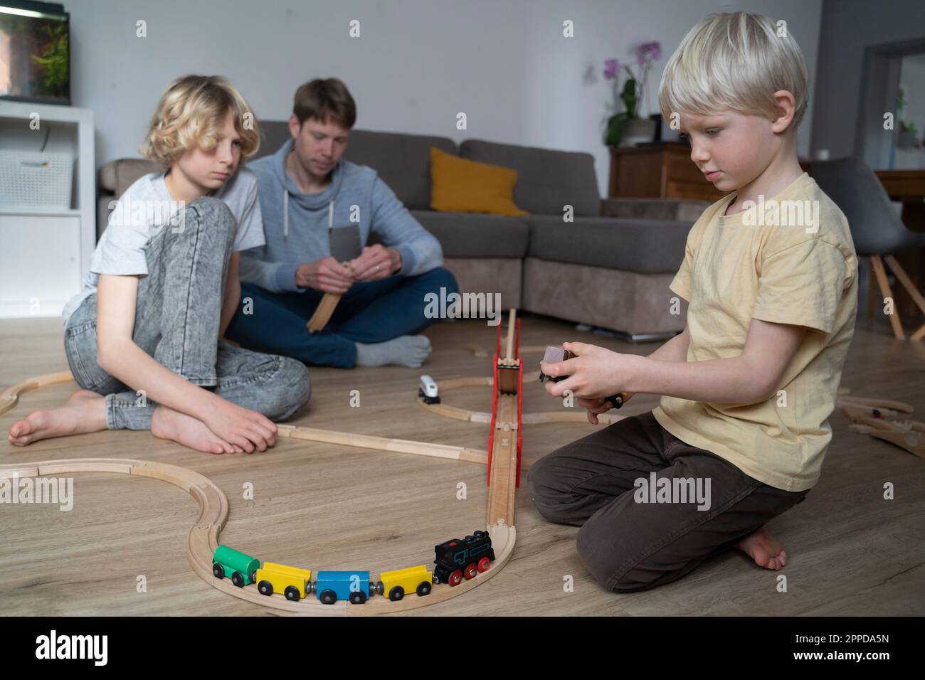 Vater und Kinder spielen zu Hause mit der Spielzeugbahn zusammen Stockfoto