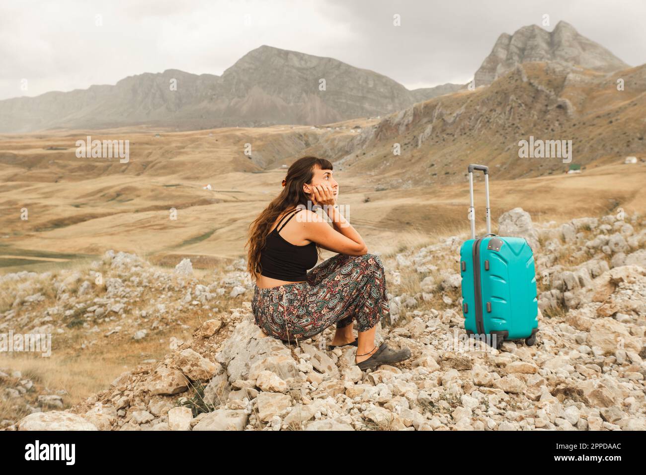Eine verwirrte Frau, die auf einem Stein sitzt, mit einem Koffer Stockfoto