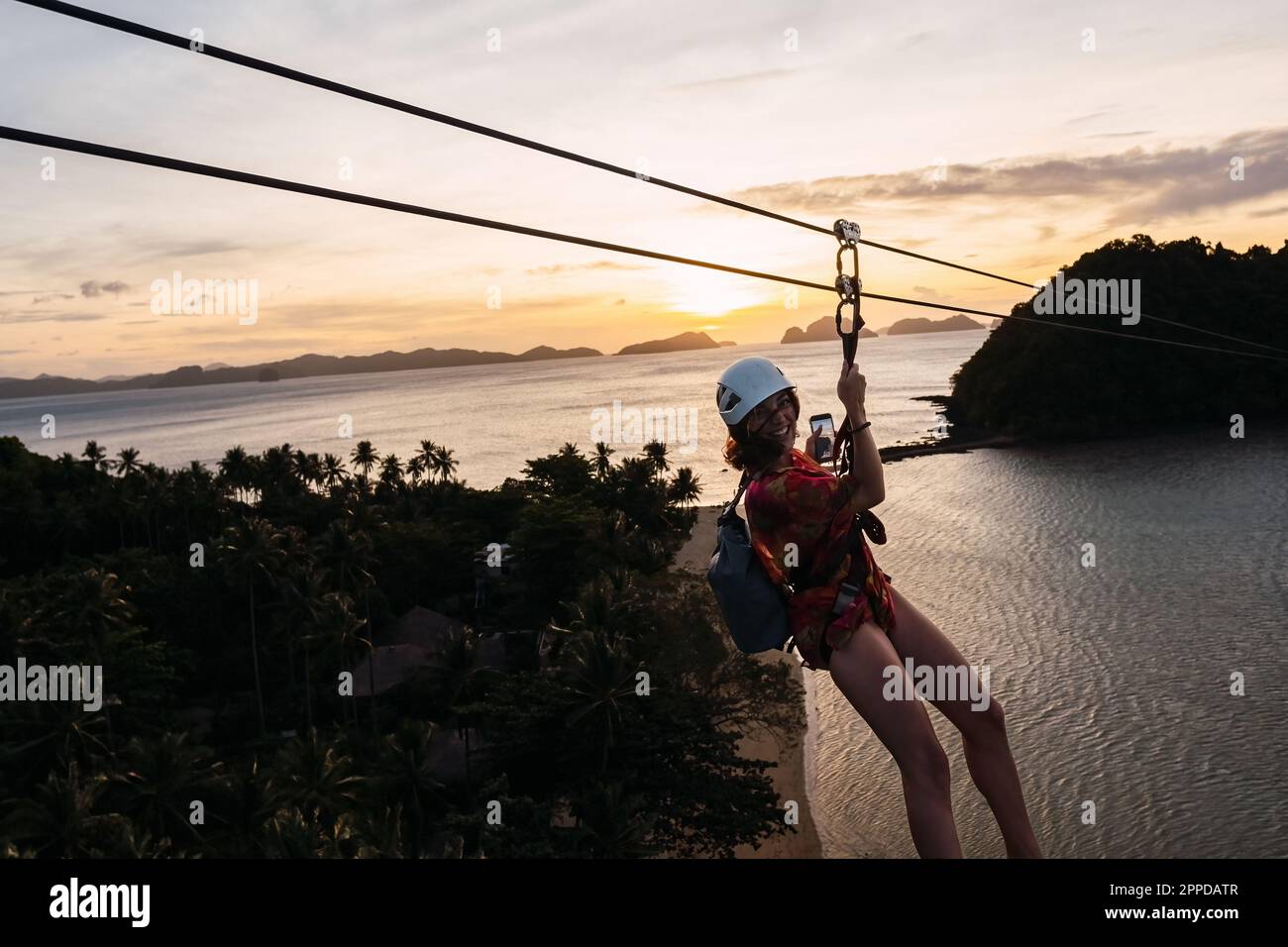 Glückliche Frau, die sich an der Seilrutsche über dem Strand bei Sonnenuntergang erfreuen kann Stockfoto