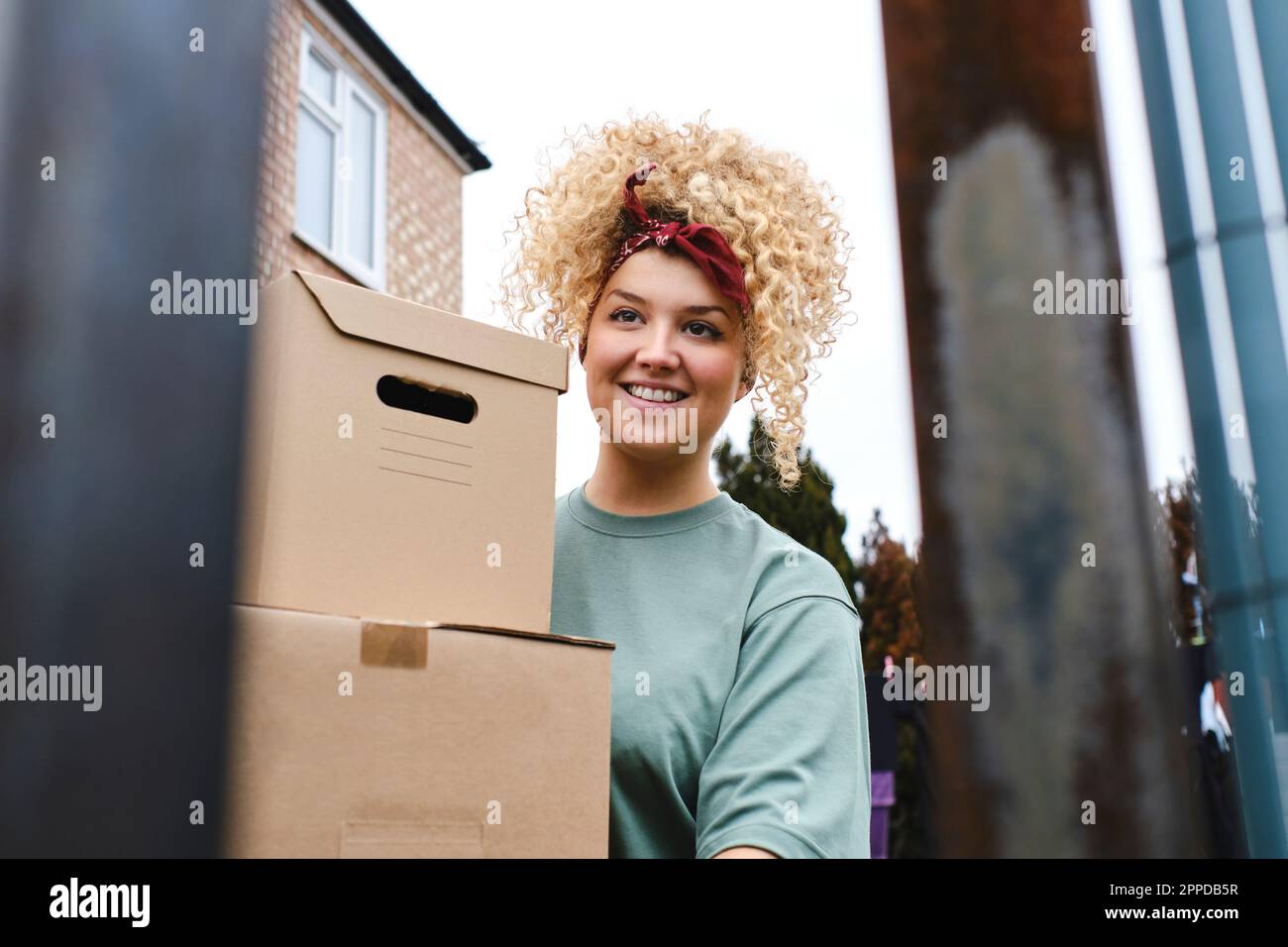 Lächelnde junge Frau mit lockigem Haar, die Pakete ausliefert Stockfoto