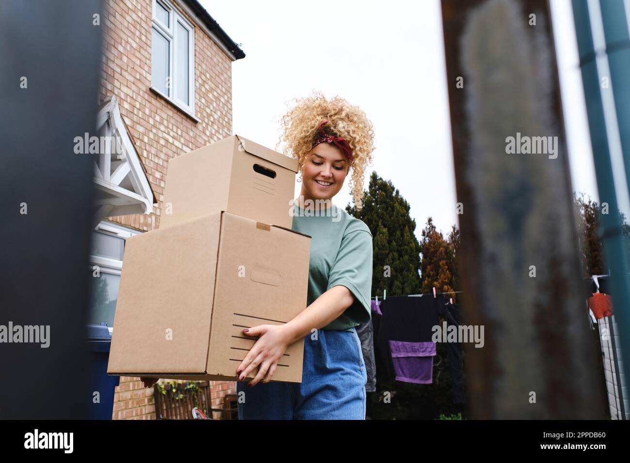 Lächelnde junge Frau mit lockigem Haar, die Pakete ausliefert Stockfoto