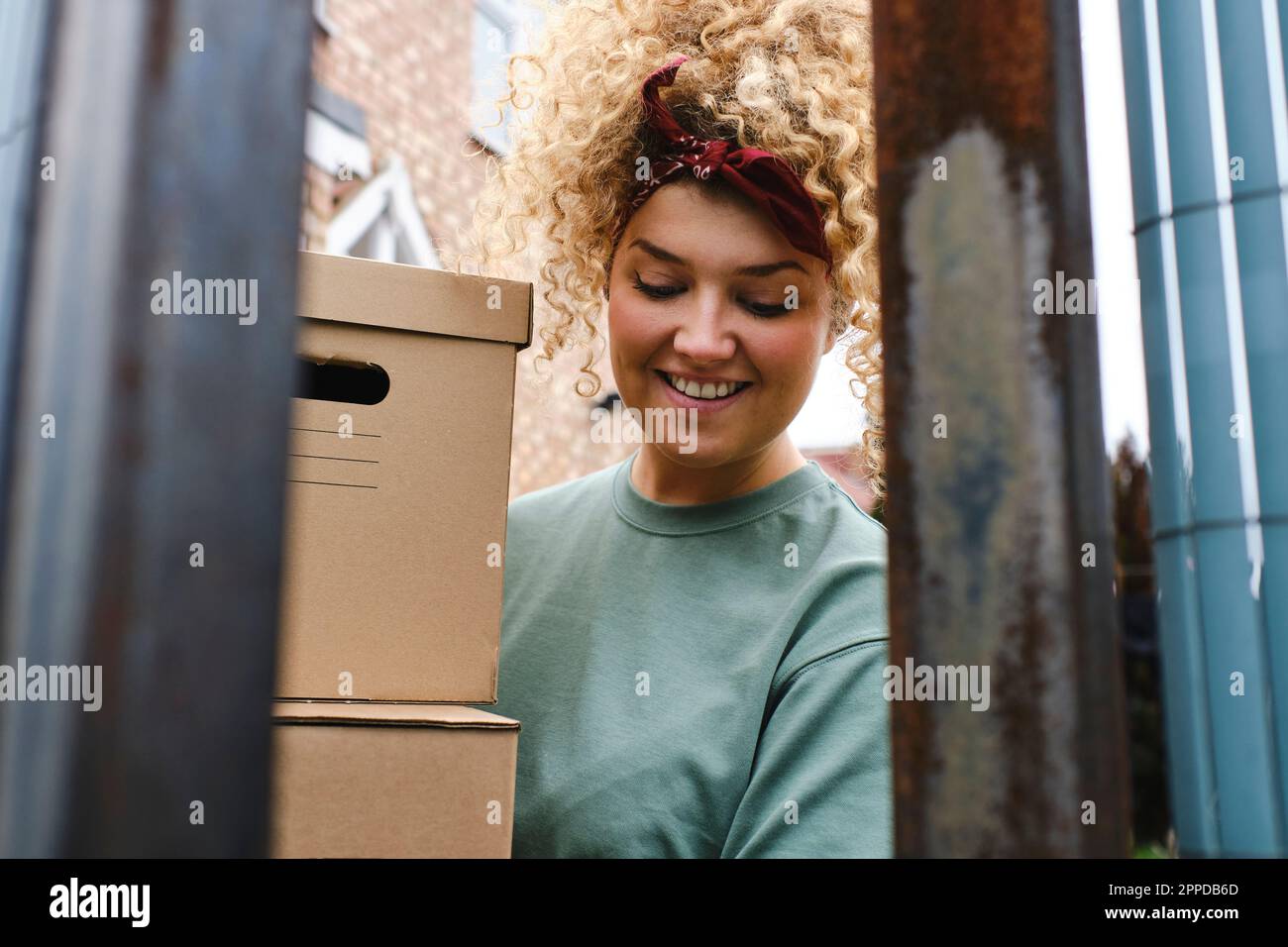 Glückliche junge Frau mit lockigem Haar, die Pakete ausliefert Stockfoto