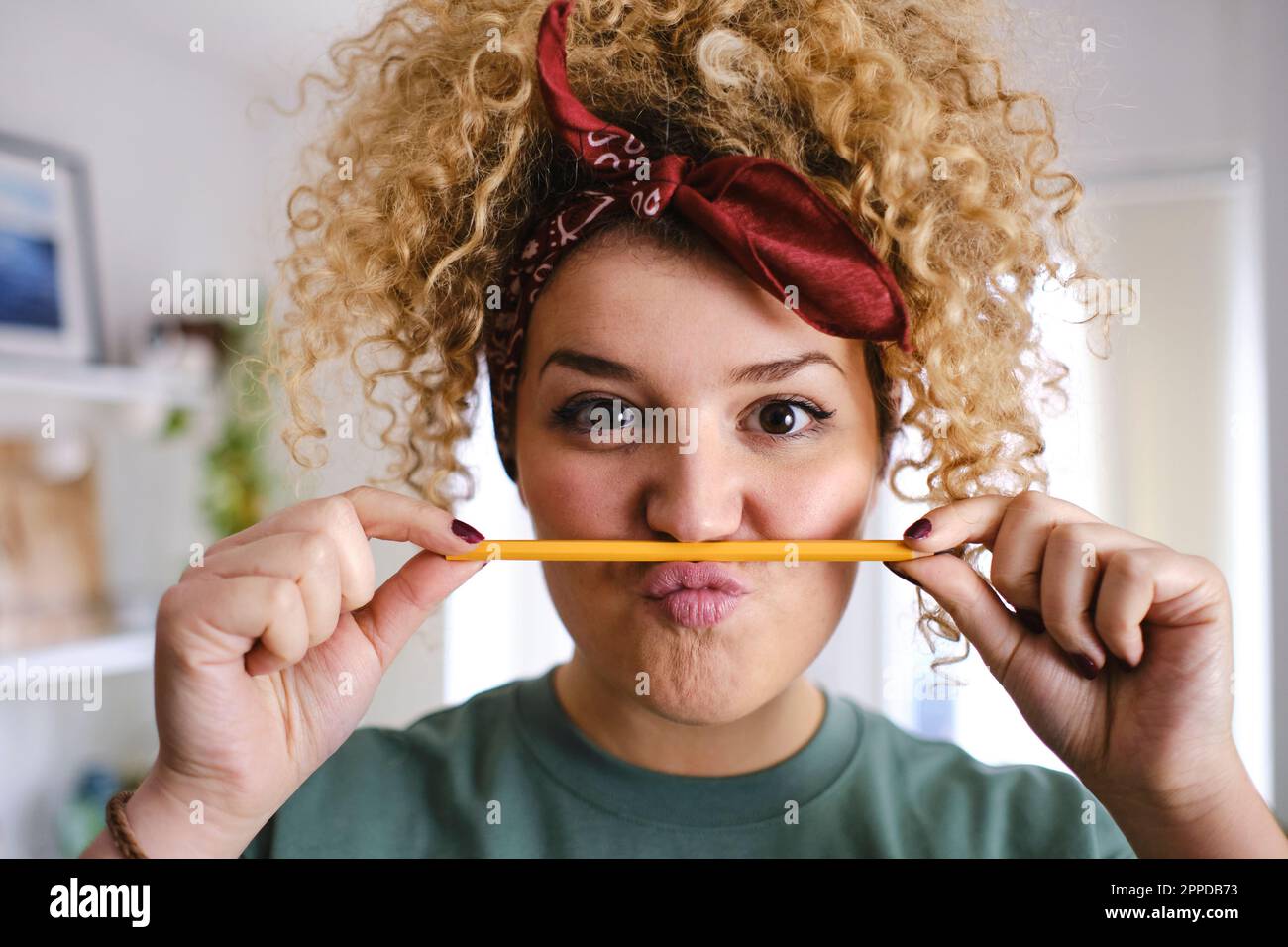 Eine junge Frau mit lockigem blondem Haar, die einen Bleistift über kotzende Lippen hält Stockfoto