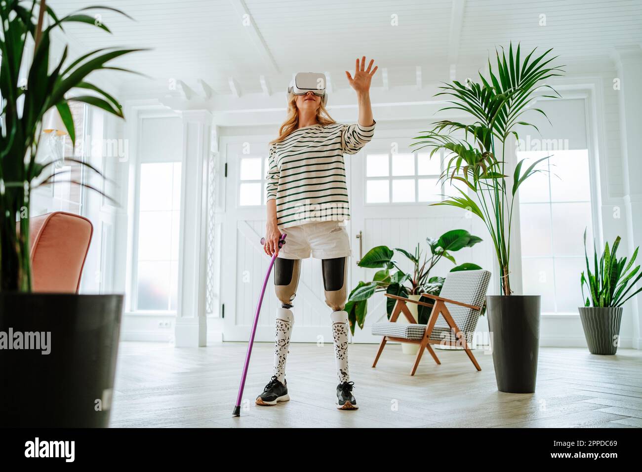 Eine Frau mit Beinprothese, die eine VR-Brille trägt und zu Hause Freizeitspiele spielt Stockfoto