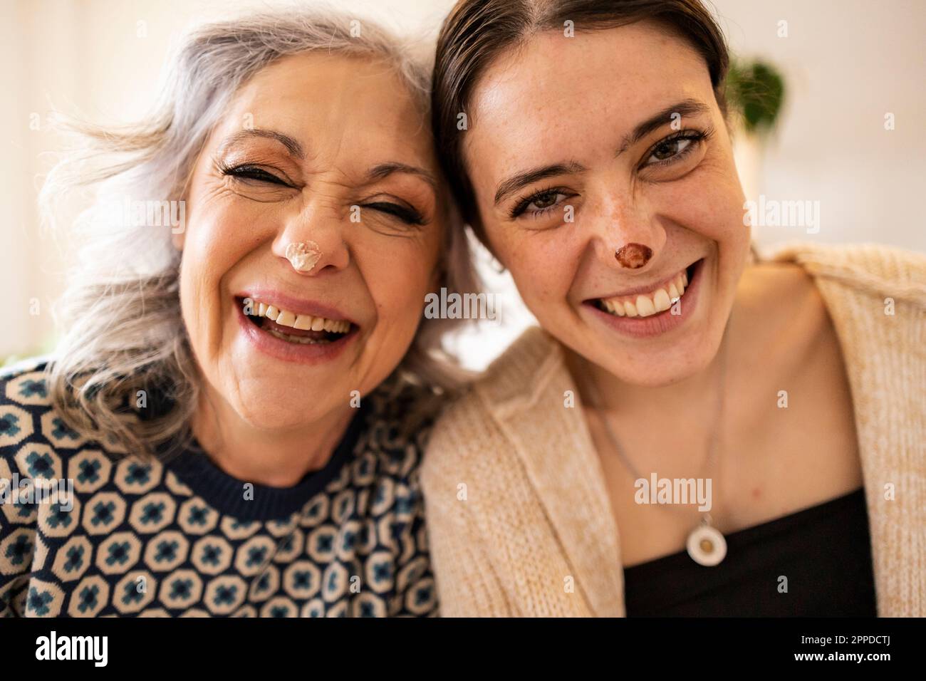 Fröhliche, reife Frau und Tochter mit Essensflecken auf der Nase, die zu Hause Spaß haben Stockfoto