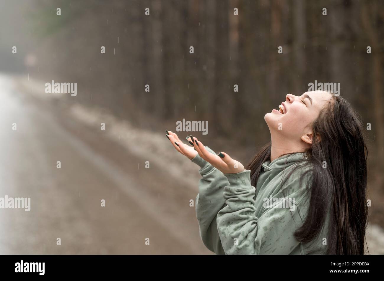 Fröhliches Teenager-Mädchen, das Regen auf der Straße genießt Stockfoto