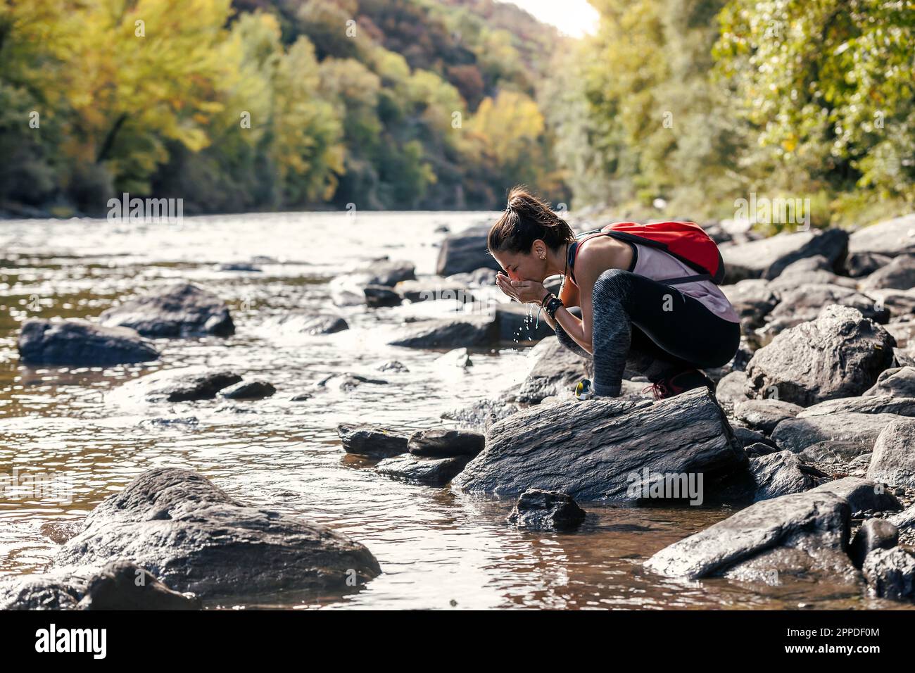 Durstige Frau, die Wasser aus dem Fluss trinkt Stockfoto