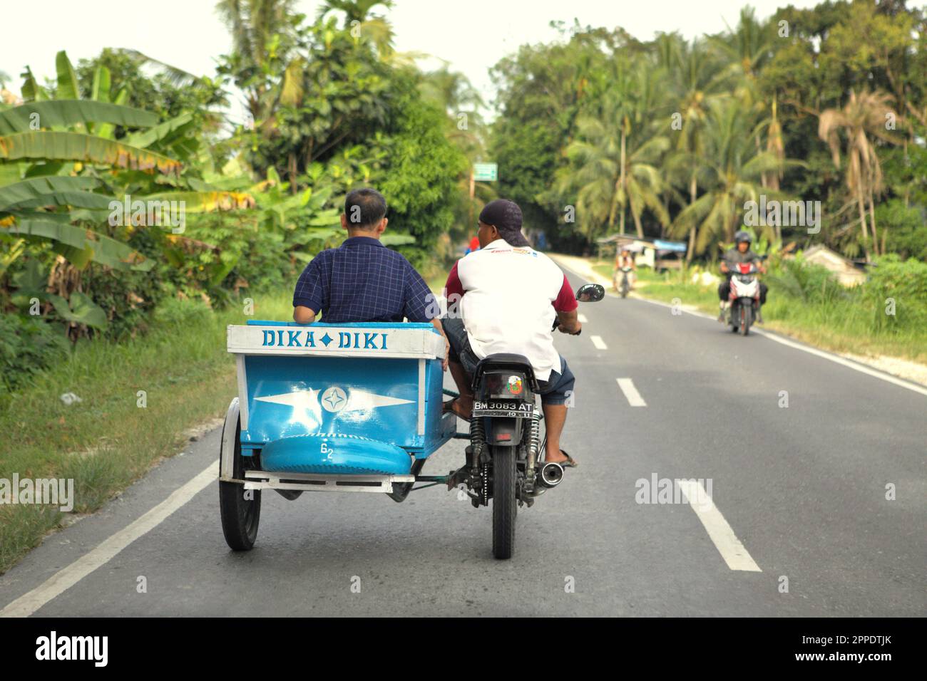 Ein Fahrer befördert einen Beifahrer auf einem Motorrad mit Beiwagen (motorisiertes Dreirad), während er auf einer Straße am Stadtrand von Pekanbaru in Riau, Indonesien, fährt. Stockfoto