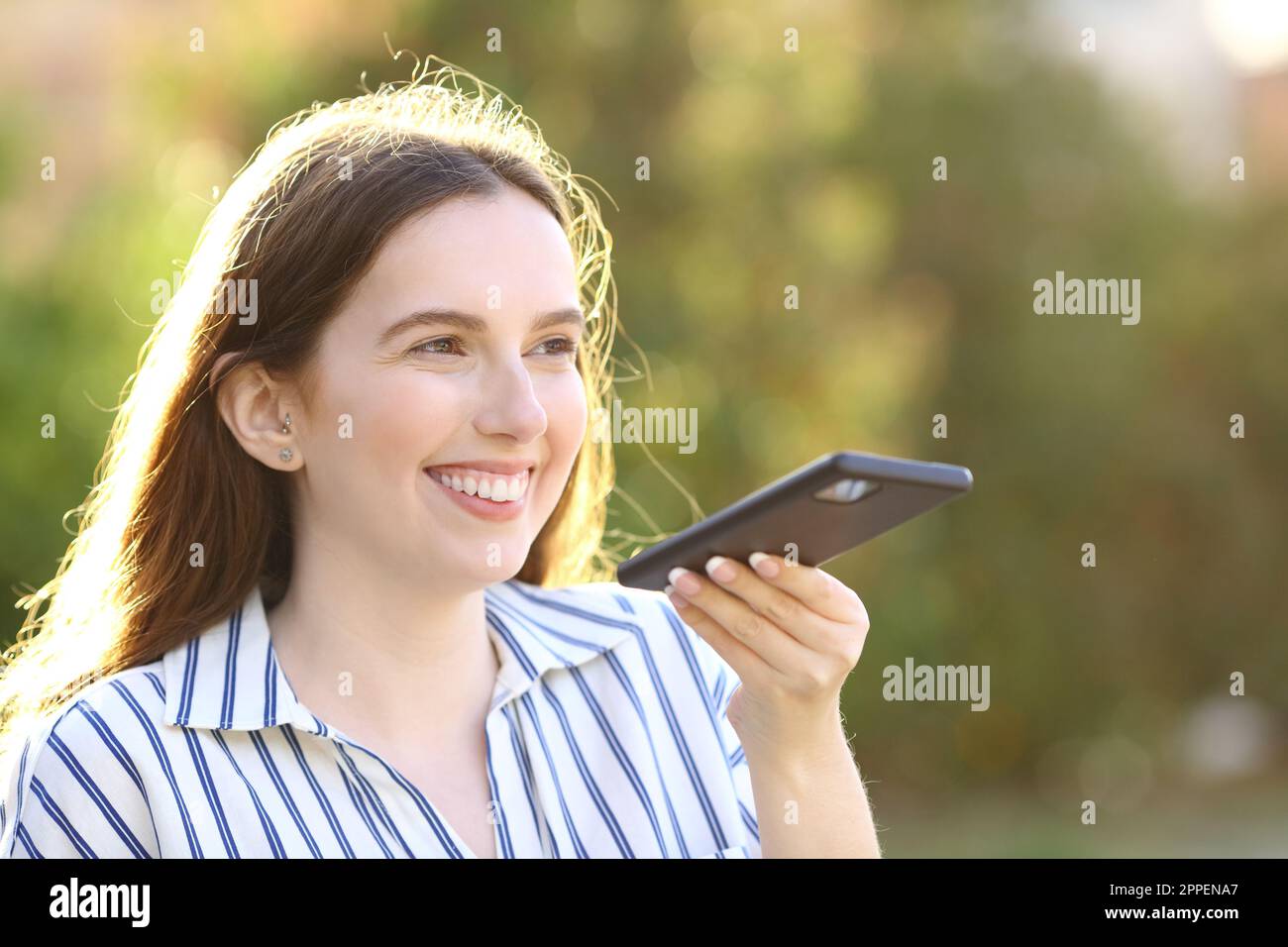 Glückliche Frau diktiert Nachricht auf dem Handy in einem Park Stockfoto