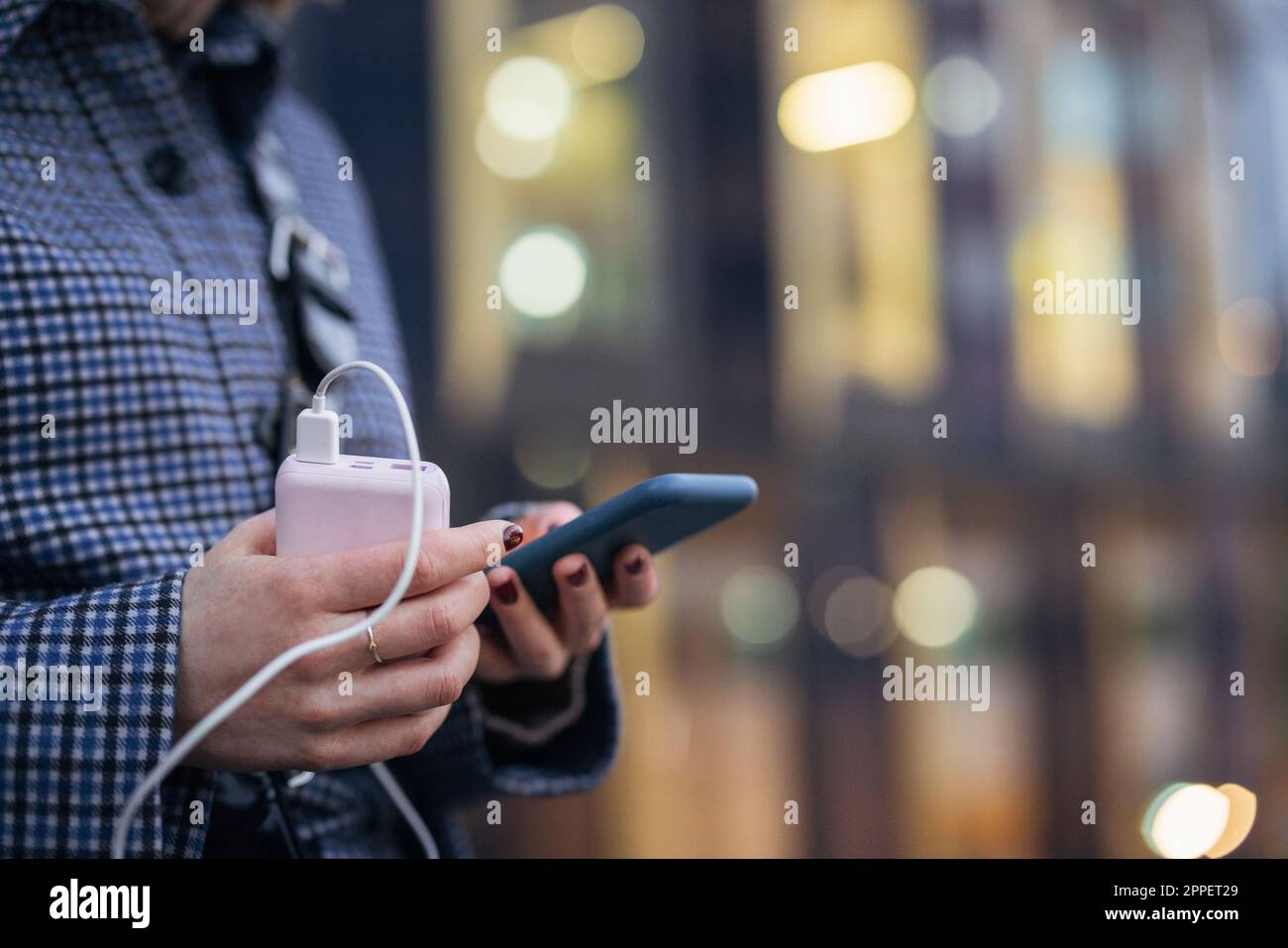 Junge Frau, die im Freien Telefon und Powerbank benutzt Stockfoto