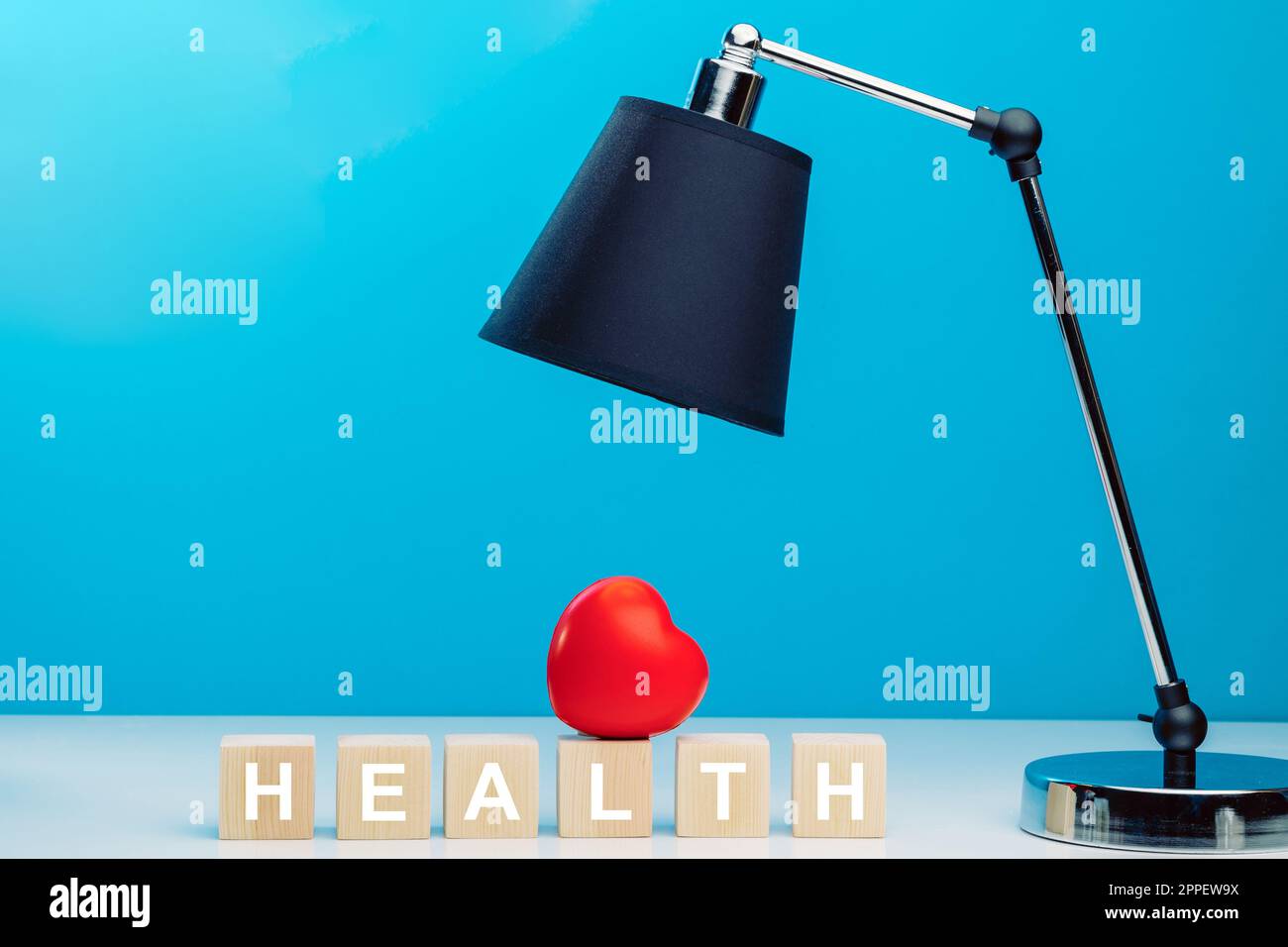 Rotes Herz auf Holzwürfeln mit dem Wort GESUNDHEIT auf einem Tisch neben einer schwarzen Tischlampe Stockfoto