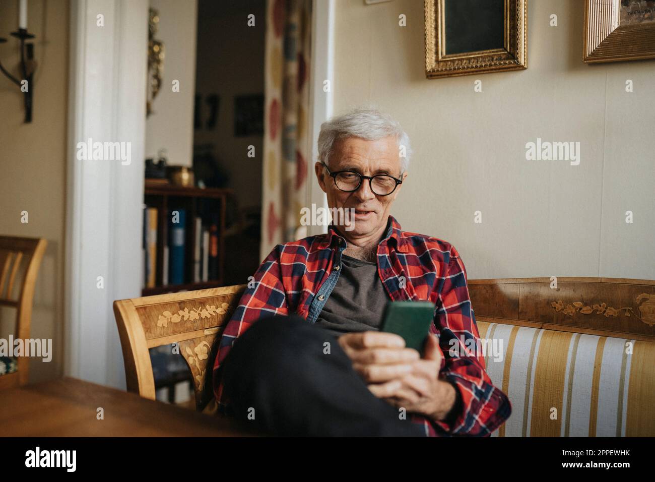 Älterer Mann, der zu Hause Smartphone benutzt Stockfoto Älterer Mann, der zu Hause Smartphone benutzt Stockfoto