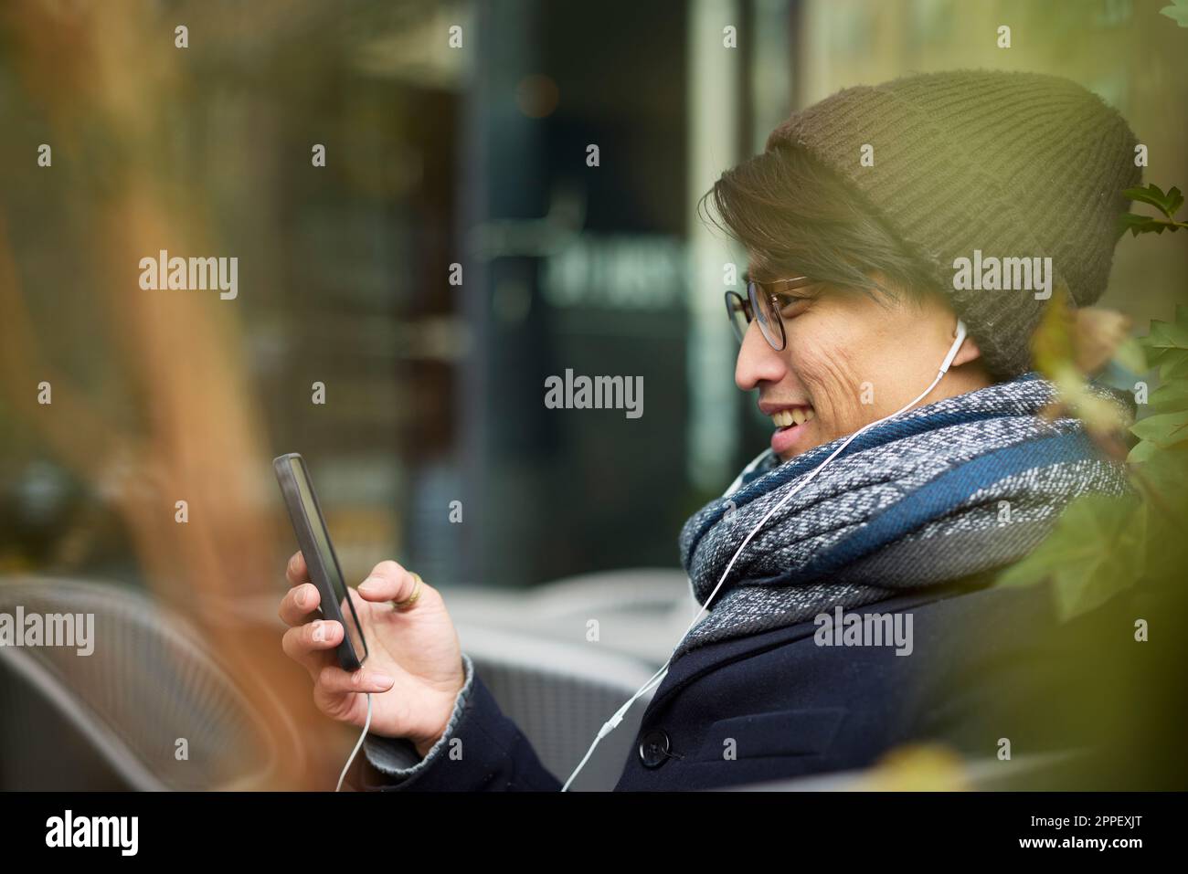 Ein Mann, der in einem Café im Freien ein Handy benutzt Stockfoto