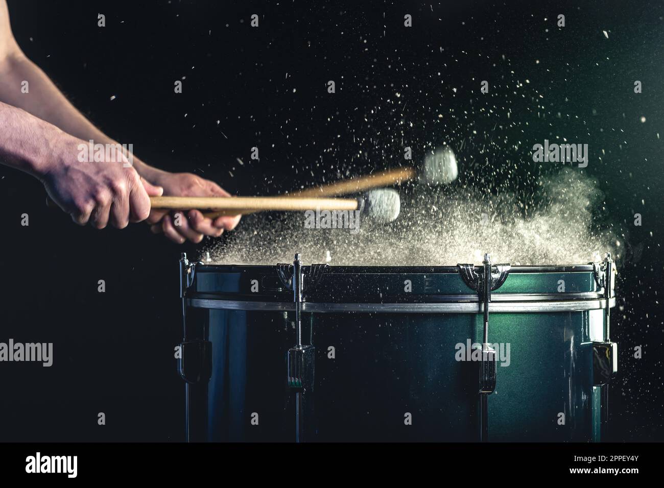 Ein Mann spielt ein musikalisches Schlaginstrument mit Stöcken auf dunklem Hintergrund. Stockfoto