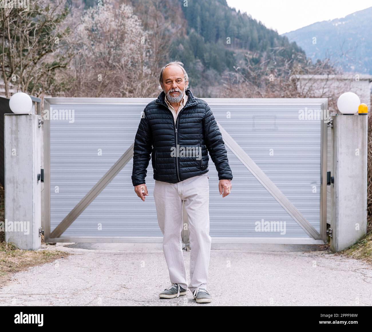 Ein Mann, der zu seinem automatischen Tor geht, von der Arbeit nach Hause kommt, die Sicherheit seines eigenen Zuhauses Stockfoto
