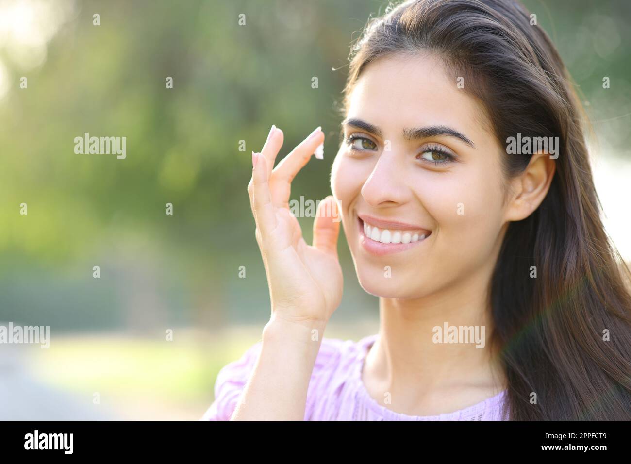 Eine schöne glückliche Frau, die im Park die Haut mit Sahne wässert Stockfoto