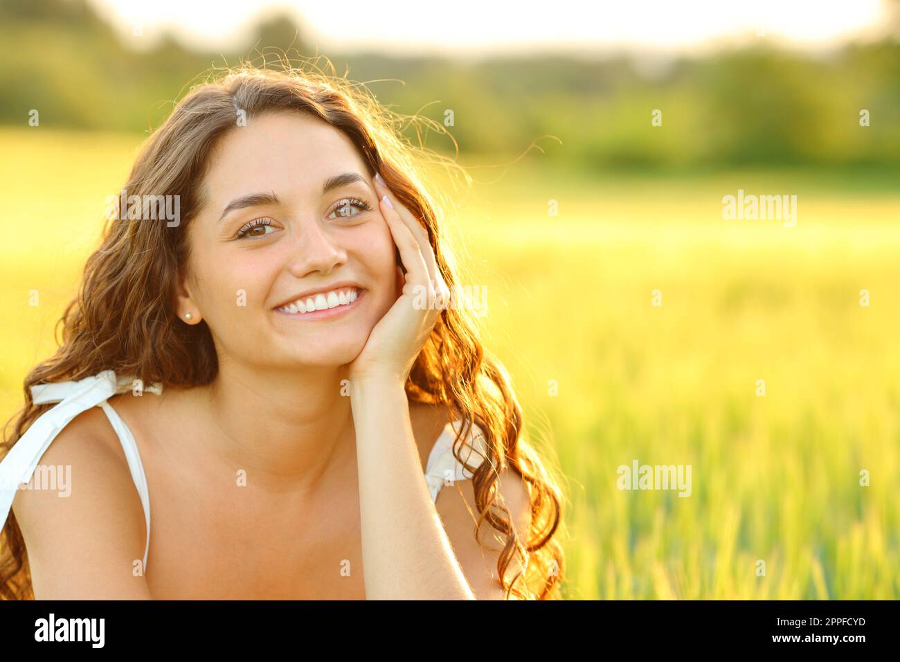 Glückliche Frau mit Schönheitslächeln, die bei Sonnenuntergang auf einem Weizenfeld posiert Stockfoto