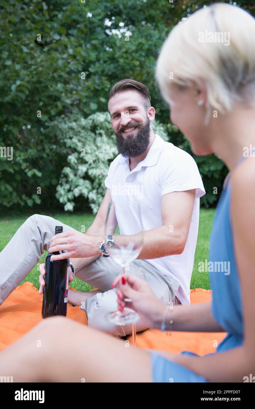 Junger Mann, der mit seiner Frau Bayern beim Picknick eine Flasche Wein öffnet Stockfoto