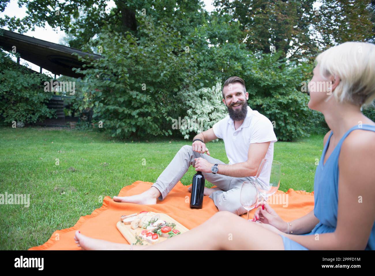 Junger Mann, der mit seiner Frau Bayern beim Picknick eine Flasche Wein öffnet Stockfoto