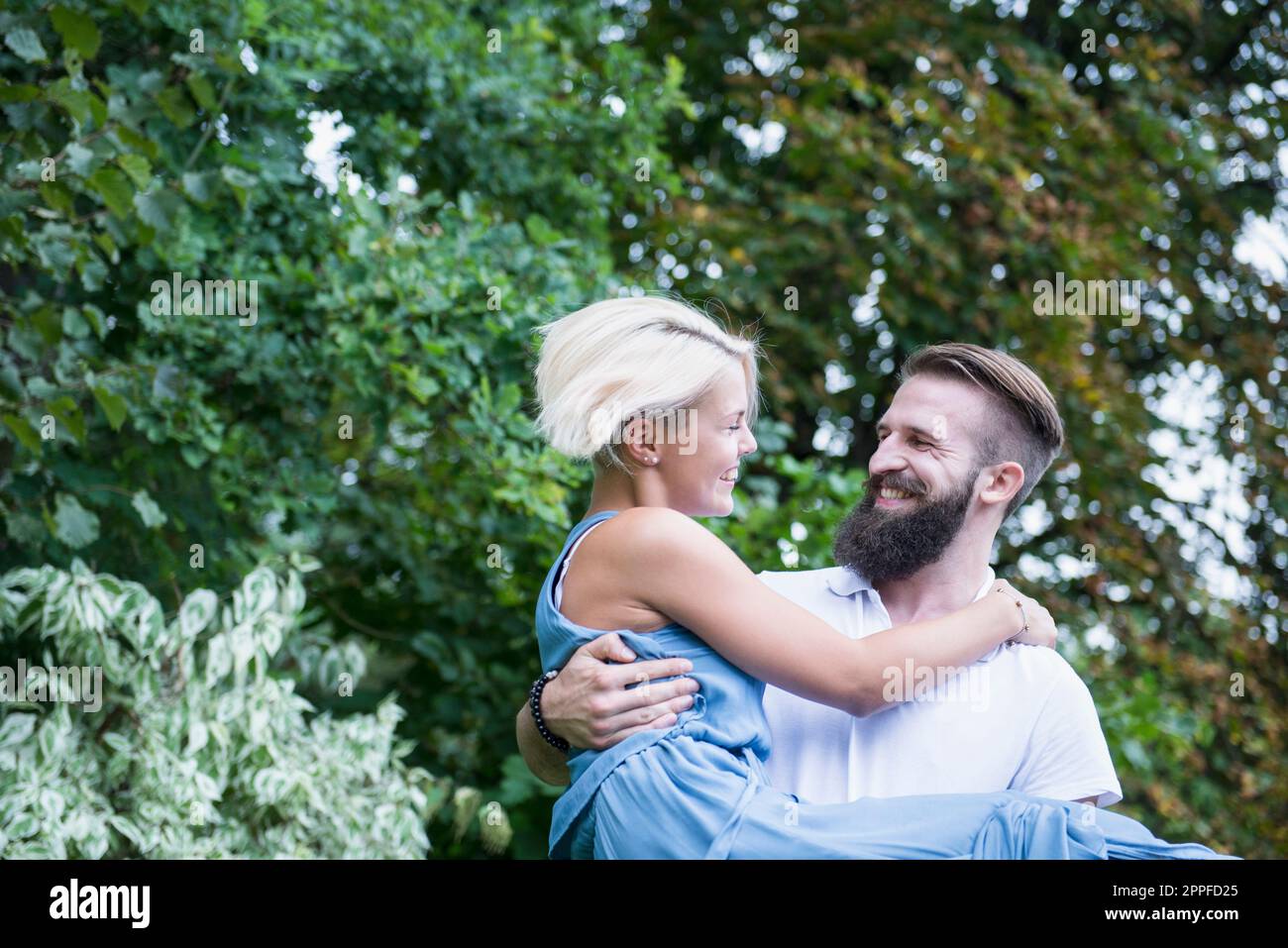 Glücklicher junger Mann, der eine Frau im Garten trägt, Bayern, Deutschland Stockfoto