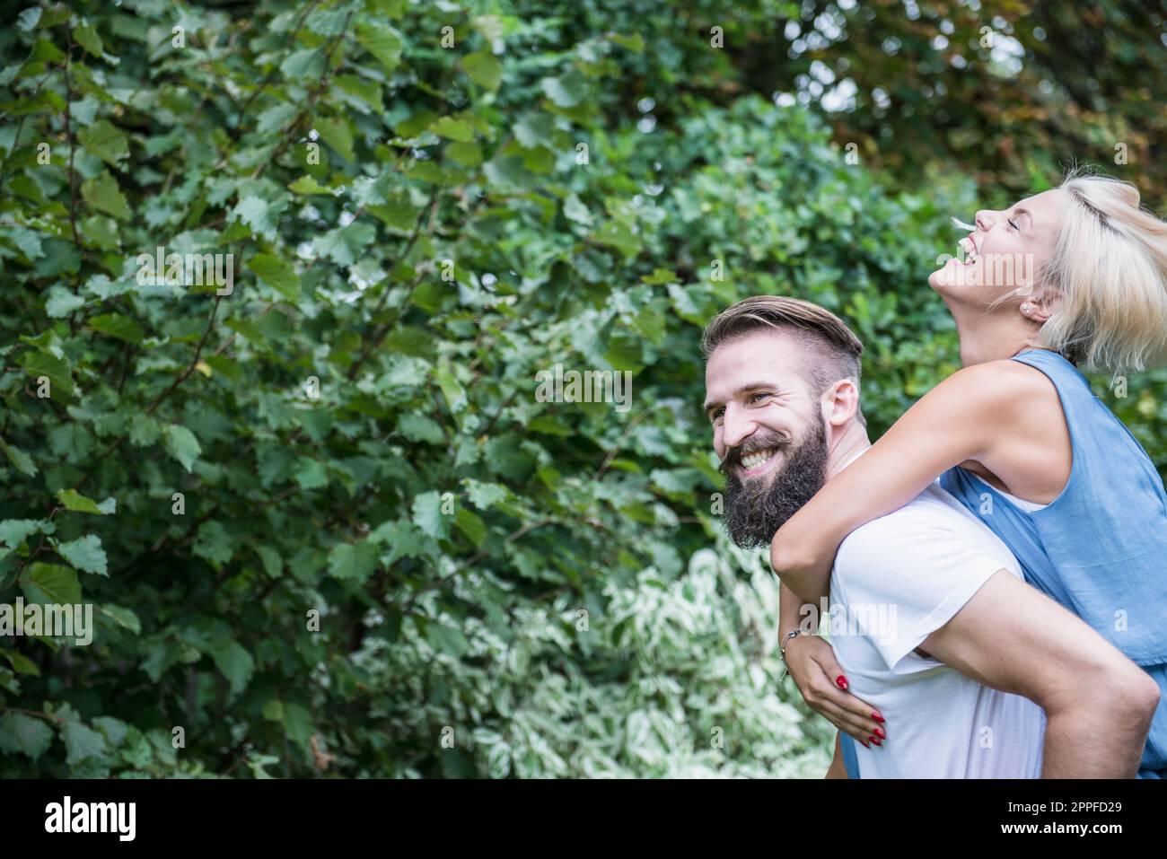 Glückliche Frau genießt Huckepackfahrt auf ihrem Freund in Garten, Bayern, Deutschland Stockfoto