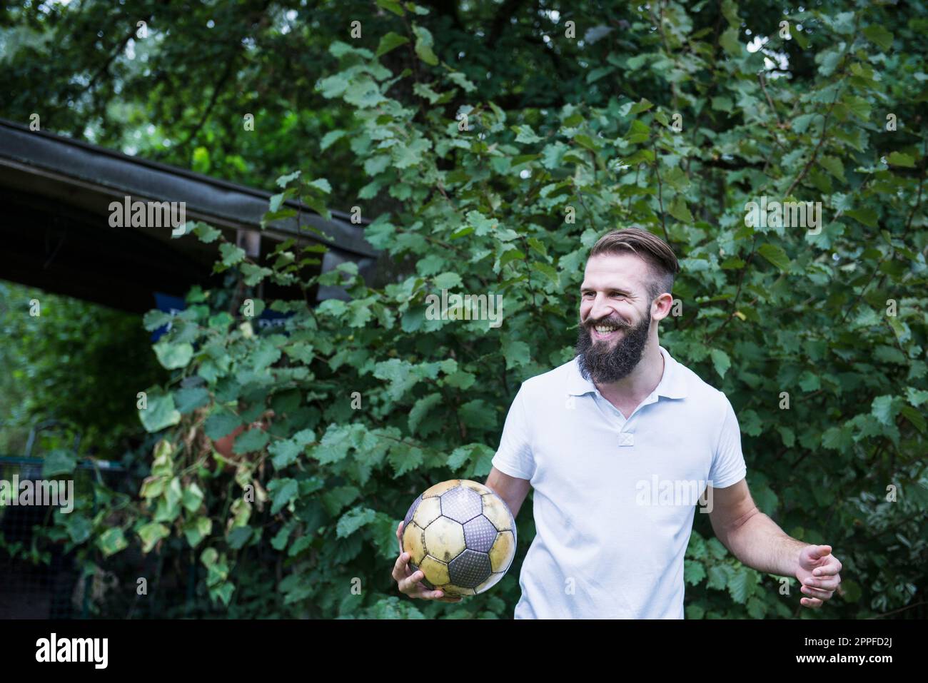 Glücklicher junger Mann, der im Garten, Bayern, Deutschland Fußball spielt Stockfoto