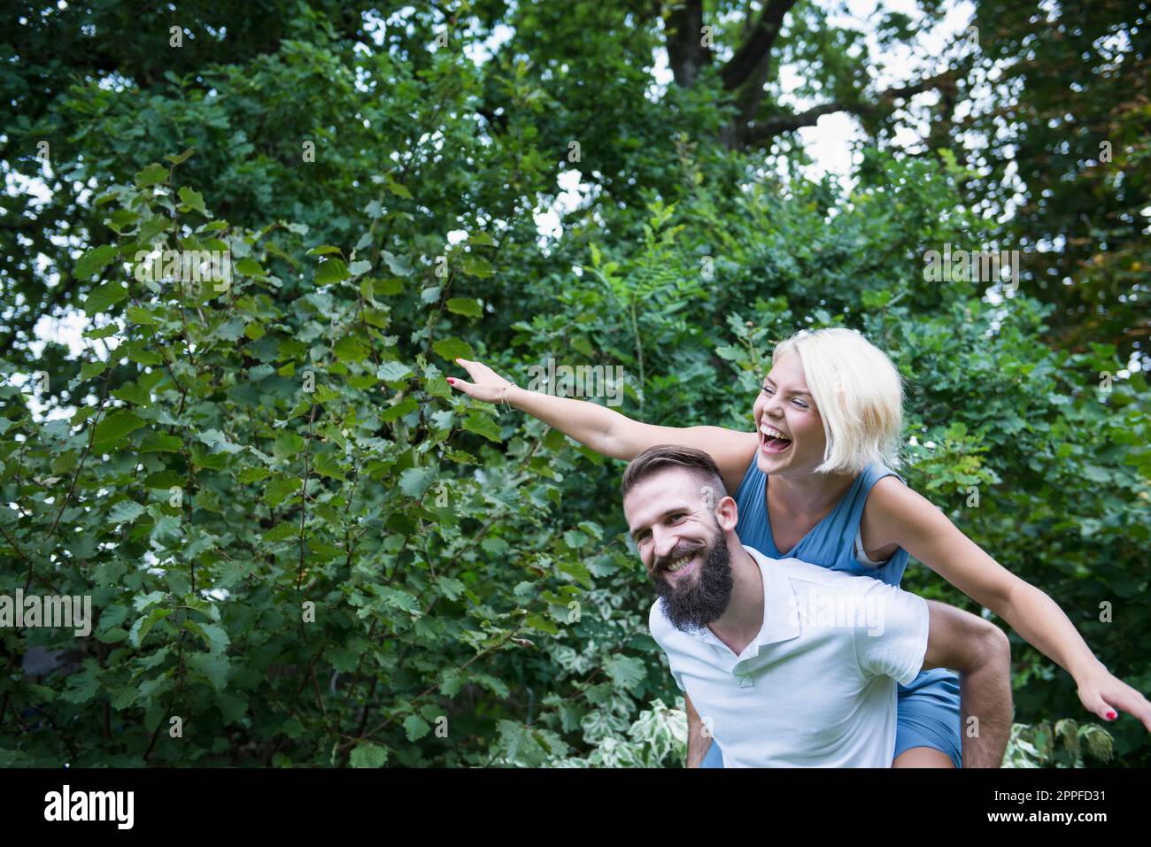 Glückliche Frau genießt Huckepackfahrt auf ihrem Freund in Garten, Bayern, Deutschland Stockfoto