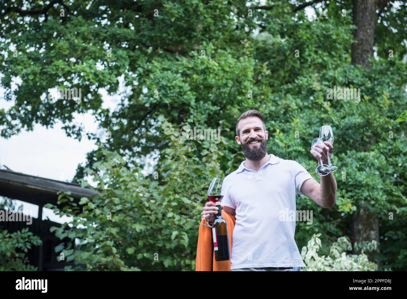 Junger Mann mit Decke und Weingläsern im Garten, Bayern, Deutschland Stockfoto