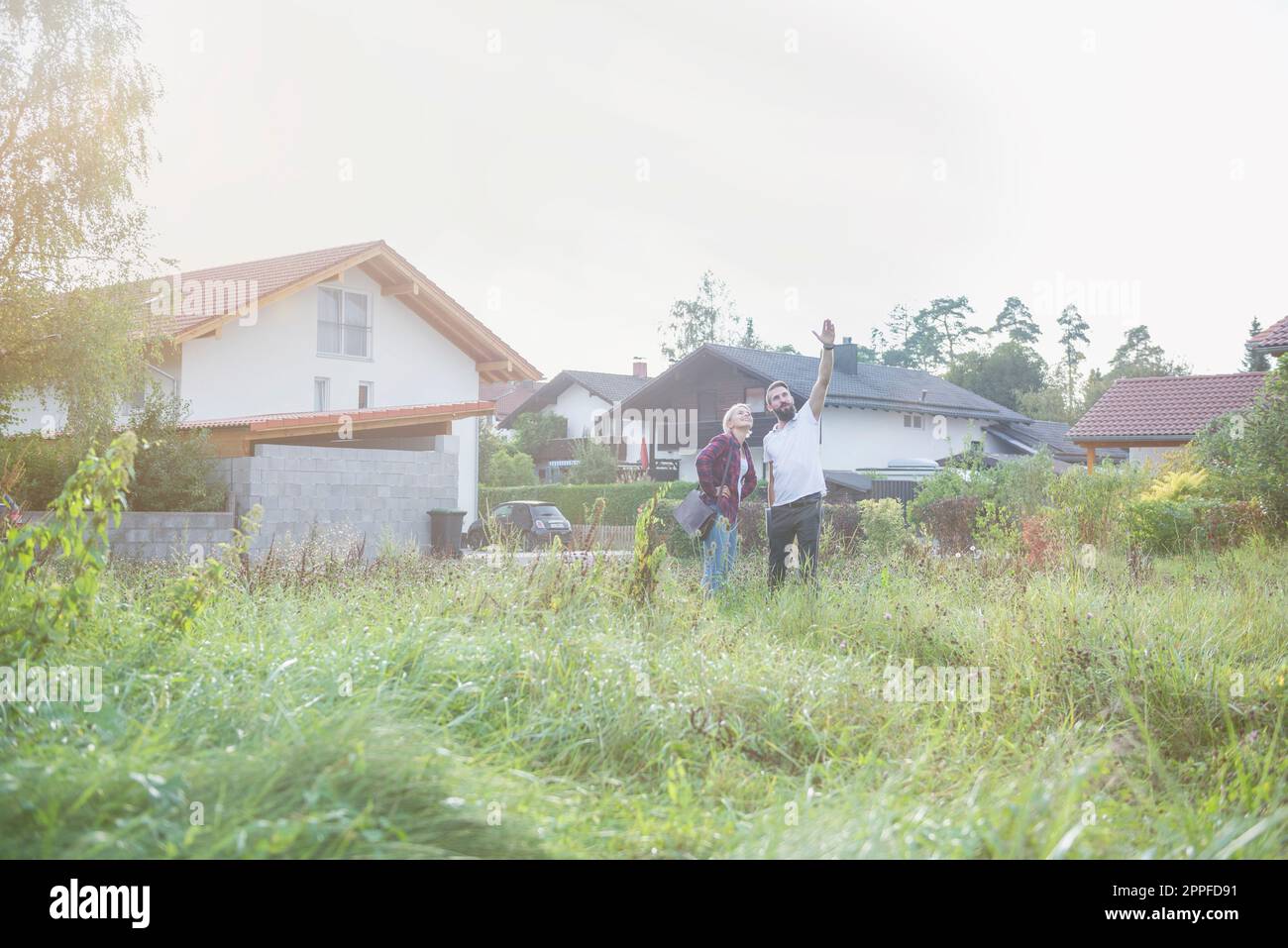 Ein junges Paar steht auf der Wiese und stellt sich ihr zukünftiges Haus vor, Bayern, Deutschland Stockfoto