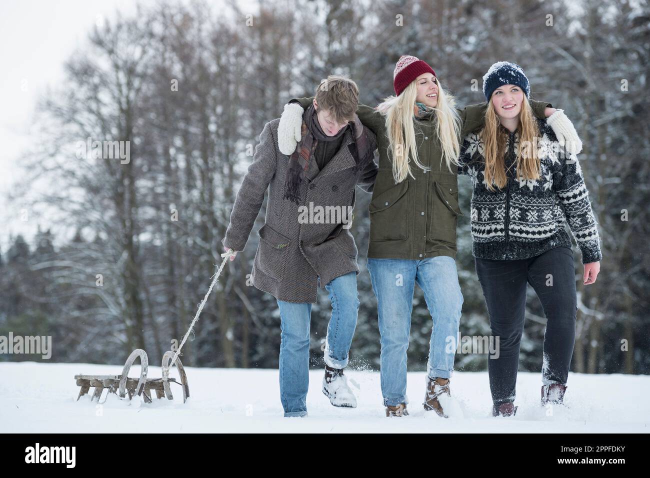 Freunde, die im Winter mit Rutsche in einer verschneiten Landschaft spazieren gehen, Bayern, Deutschland Stockfoto