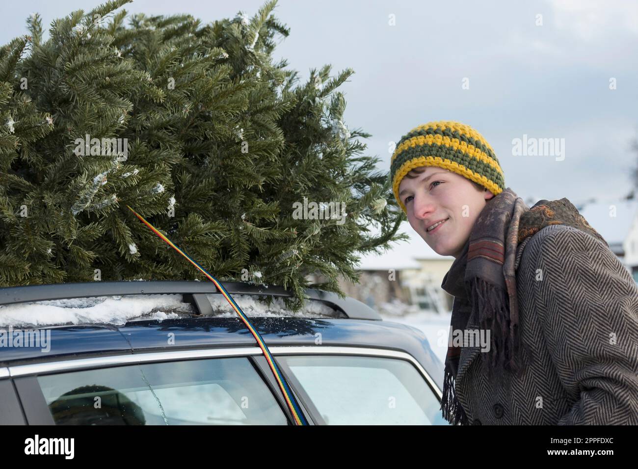 Junger Mann, der den weihnachtsbaum auf dem Dach seines Autos schnallt, Bayern, Deutschland Stockfoto