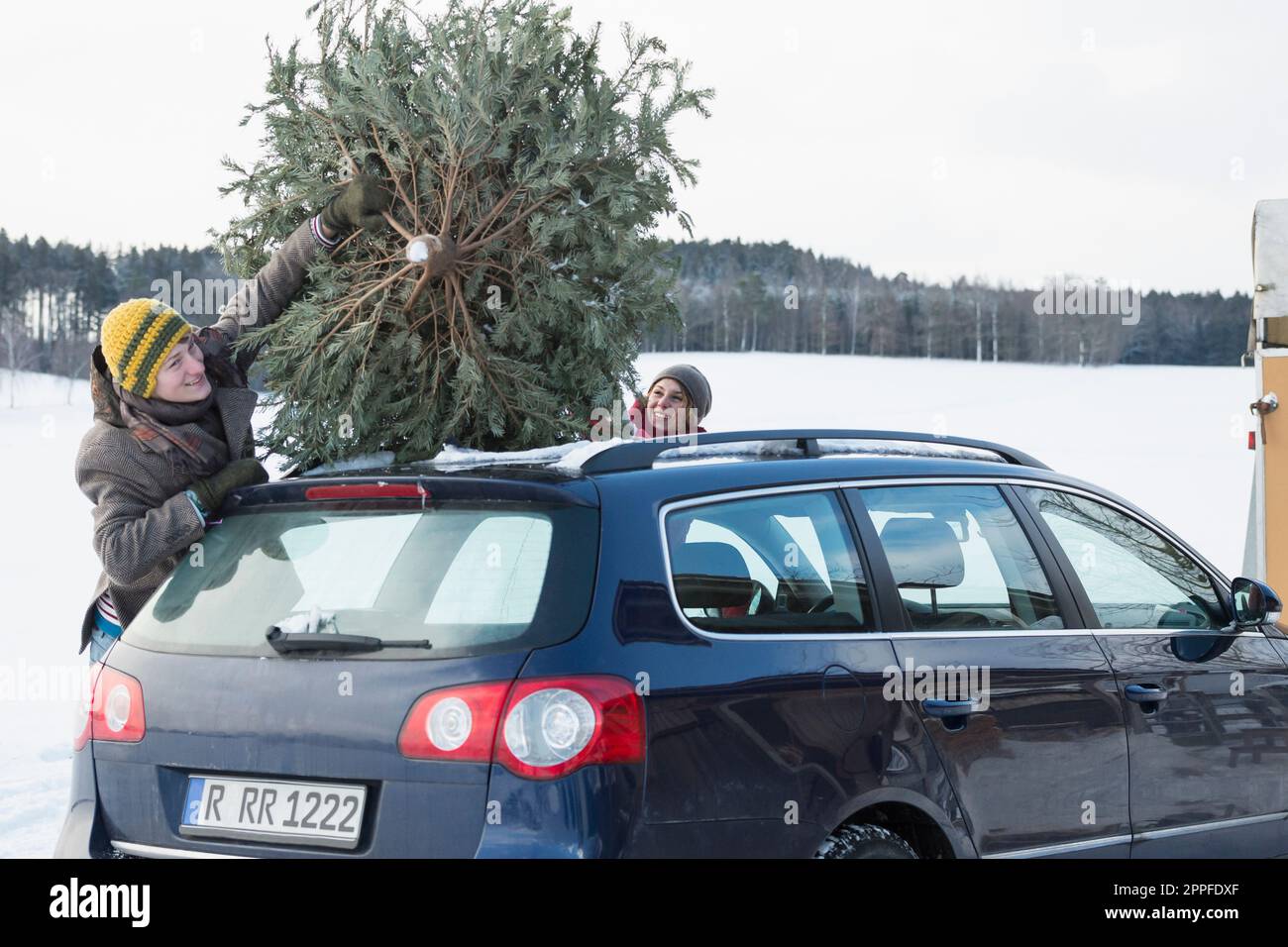 Ein junges Paar, das den weihnachtsbaum auf dem Autodach bindet, Bayern, Deutschland Stockfoto