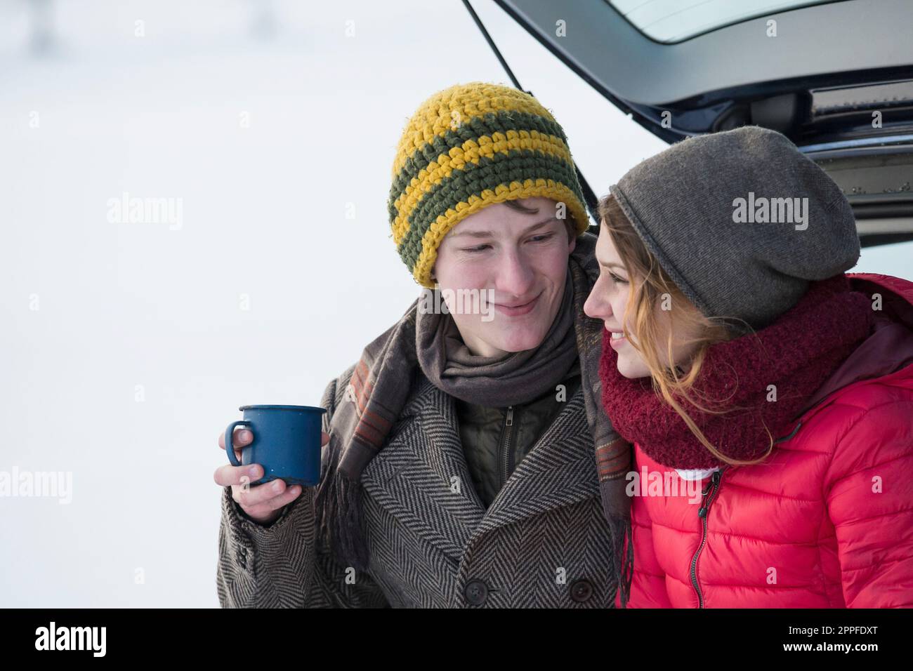 Ein junges Paar, das im Winter mit einer Kaffeetasse im Kofferraum eines Autos sitzt, Bayern, Deutschland Stockfoto