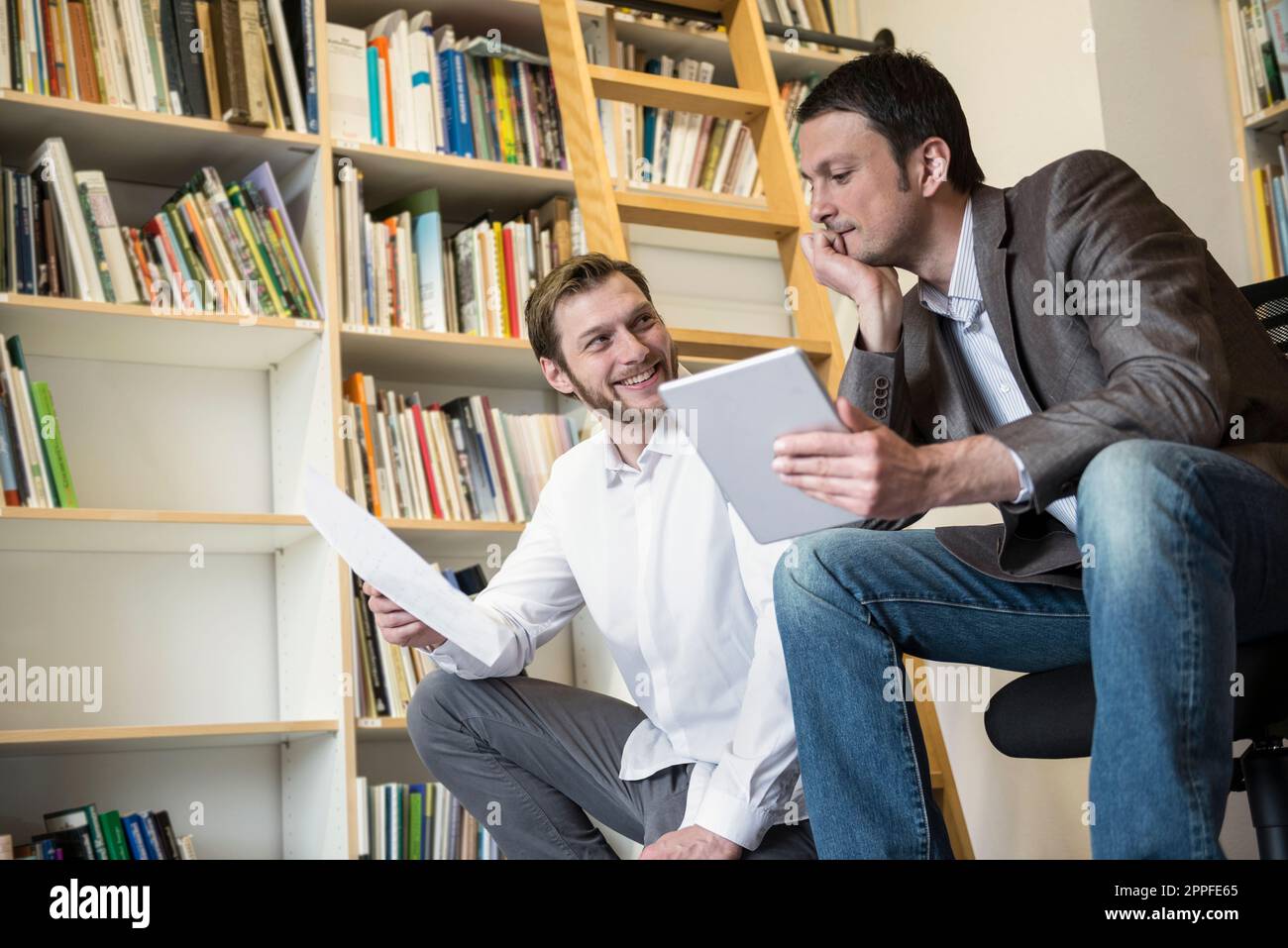 Zwei Geschäftsleute, die sich Notizen ansehen und ein digitales Tablet in einem Büro in Bayern verwenden Stockfoto