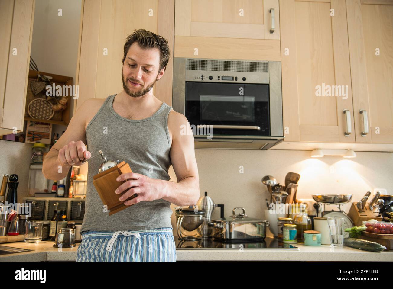 Mann steht in der Küche und mahlt Kaffeemühle, München, Bayern, Deutschland Stockfoto