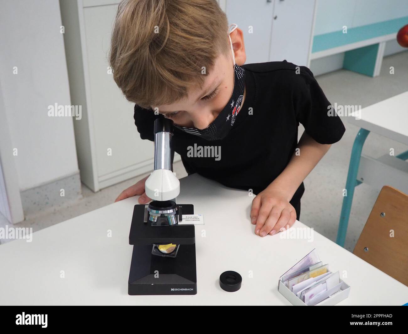 Sremska Mitrovica, Serbien, 15. Mai 2021. Ein 8-jähriger Junge in einem schwarzen T-Shirt sieht mit einem Auge durch ein Mikroskop aus. Biologiestunde. Der Unterrichtsvorgang bei Kindern. Schulunterricht Stockfoto