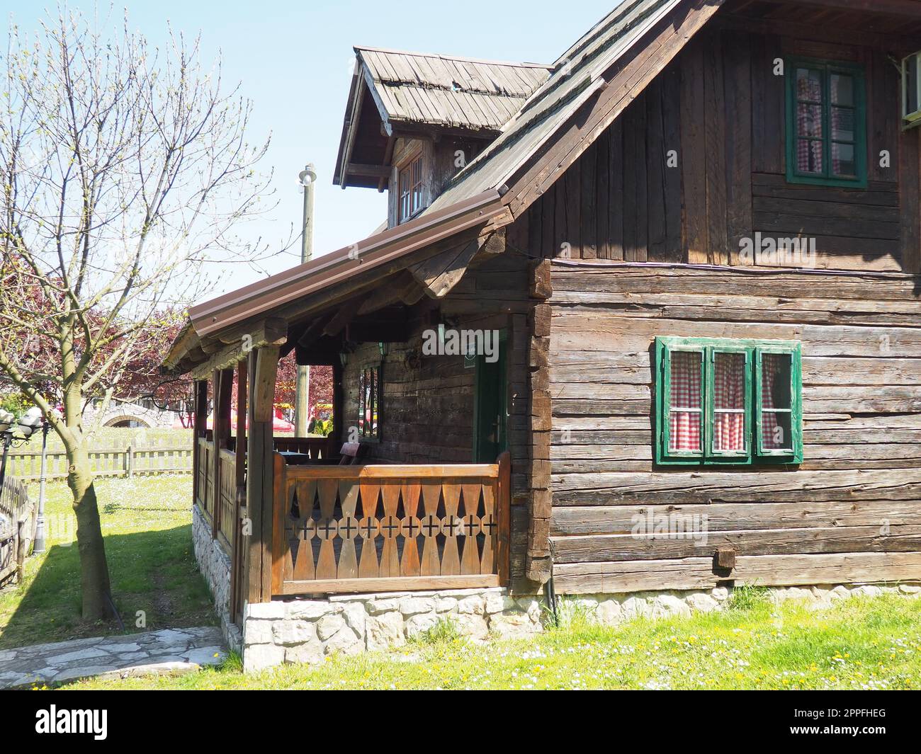 Traditionelles Wohnhaus im bosnischen Gebirge aus dem 19. Jahrhundert. Restauriertes Ethno-Gebäude, Holzterrasse, Küchenvorhänge mit Karomuster Stockfoto