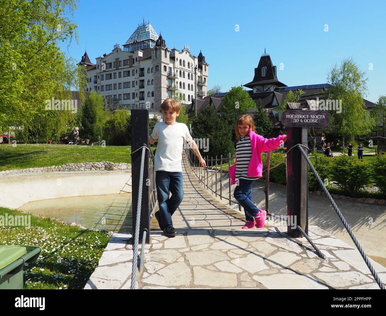 Stanisici, Bijelina, Bosnien und Herzegowina April 25 2021 Ein Junge im Alter von 8 Jahren und ein Mädchen im Alter von 7 Jahren, Bruder und Schwester, stehen an der Hängebrücke im Dorf Ethno. Kinder besuchen Sehenswürdigkeiten Stockfoto