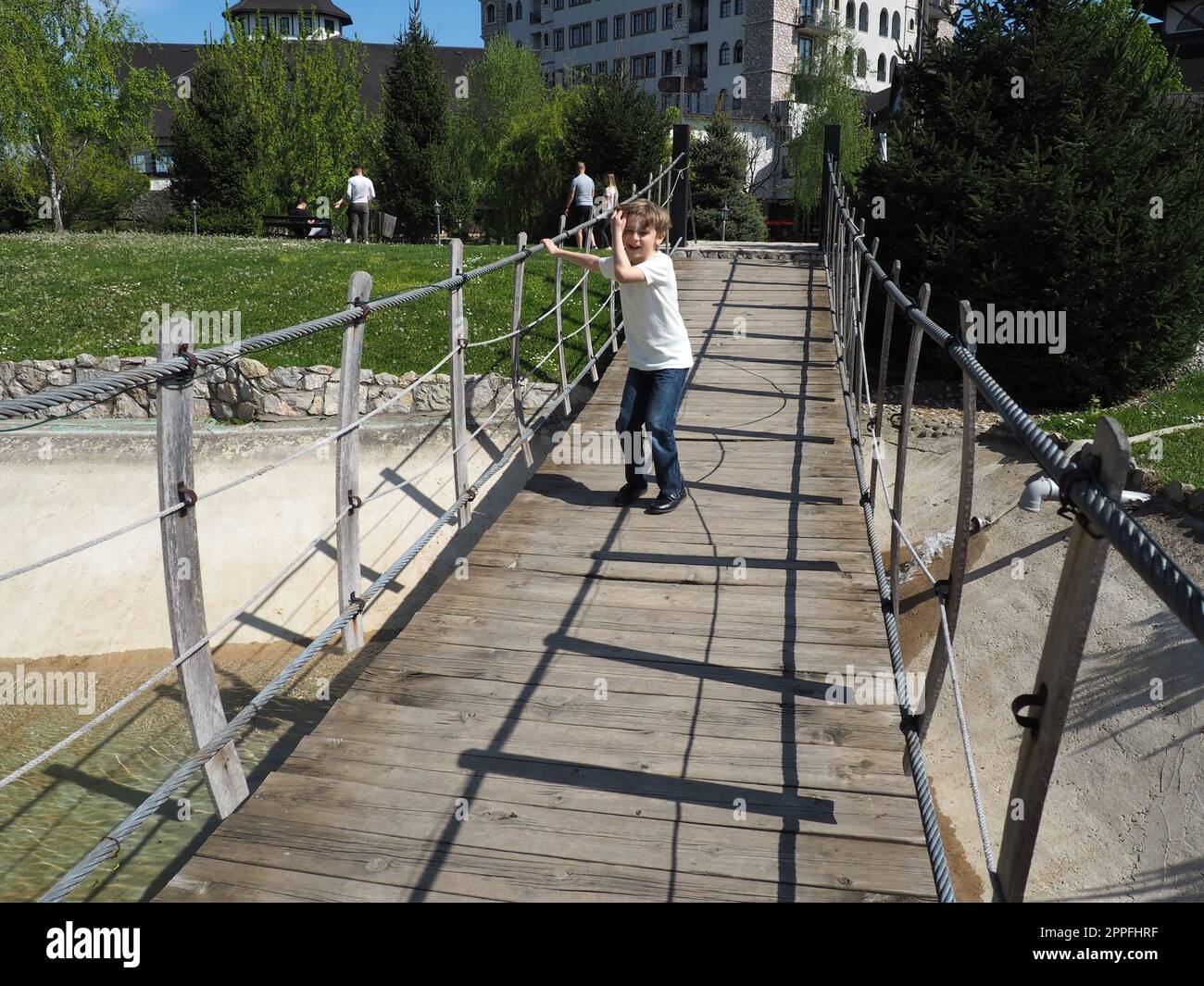 Hängende Holzbrücke. Der Junge versucht, die Brücke zu rocken. Stanisici, Bijelina, Bosnien und Herzegowina. Eine Brücke aus Brettern und Geländern, die von 4 Personen getragen werden kann. Stockfoto