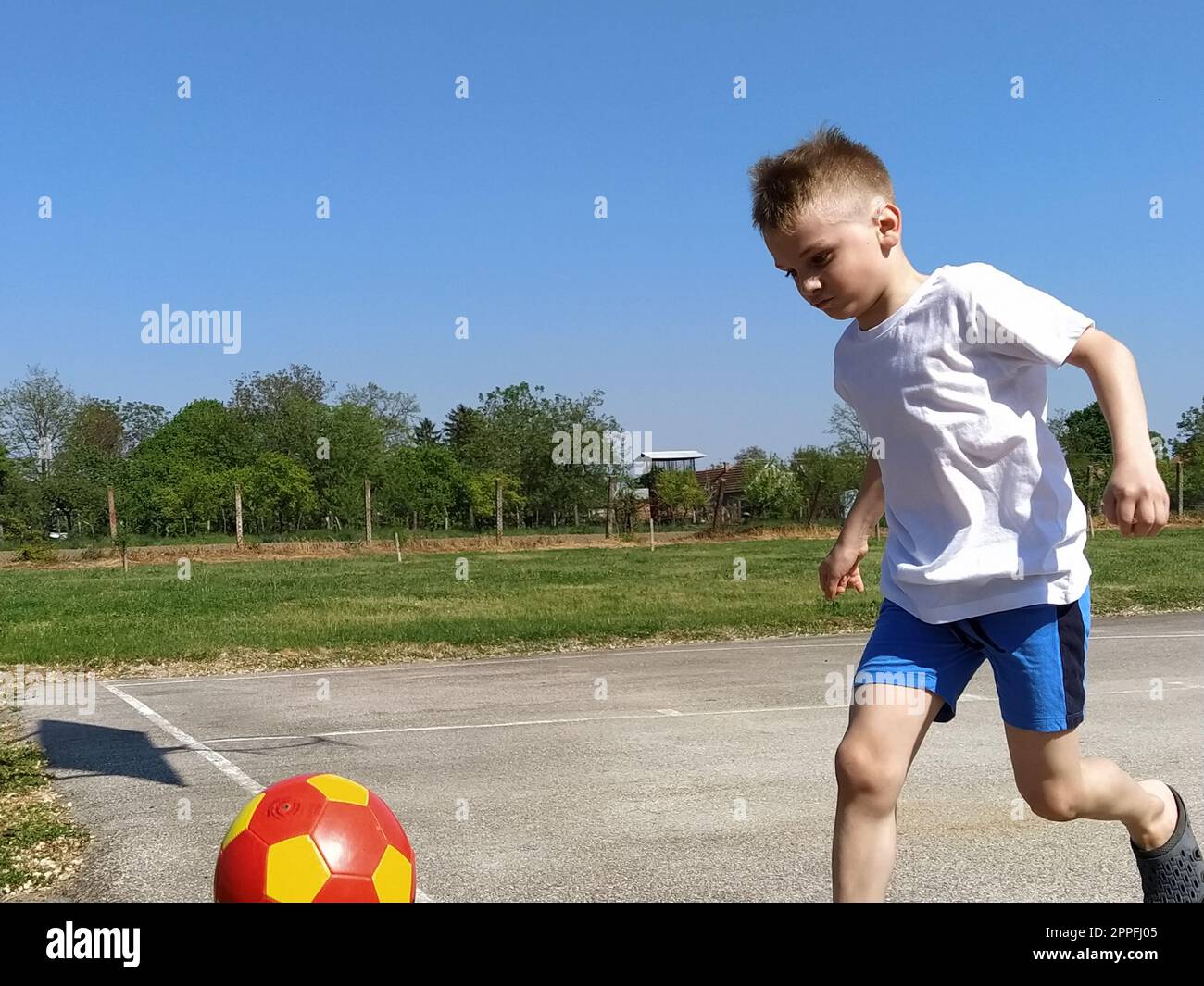 Ein Junge läuft einem Basketballball hinterher. Das Kind spielt mit einem Ball auf dem Spielplatz. Geben Sie Platz für Text frei. Blauer Himmel im Hintergrund. Ein blondes Kind Stockfoto