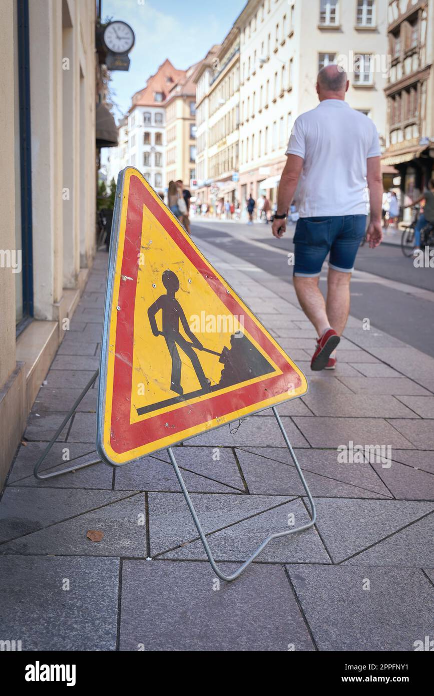 Baustellenschild und Passanten auf einem Bürgersteig in der Innenstadt von Straßburg, Frankreich Stockfoto