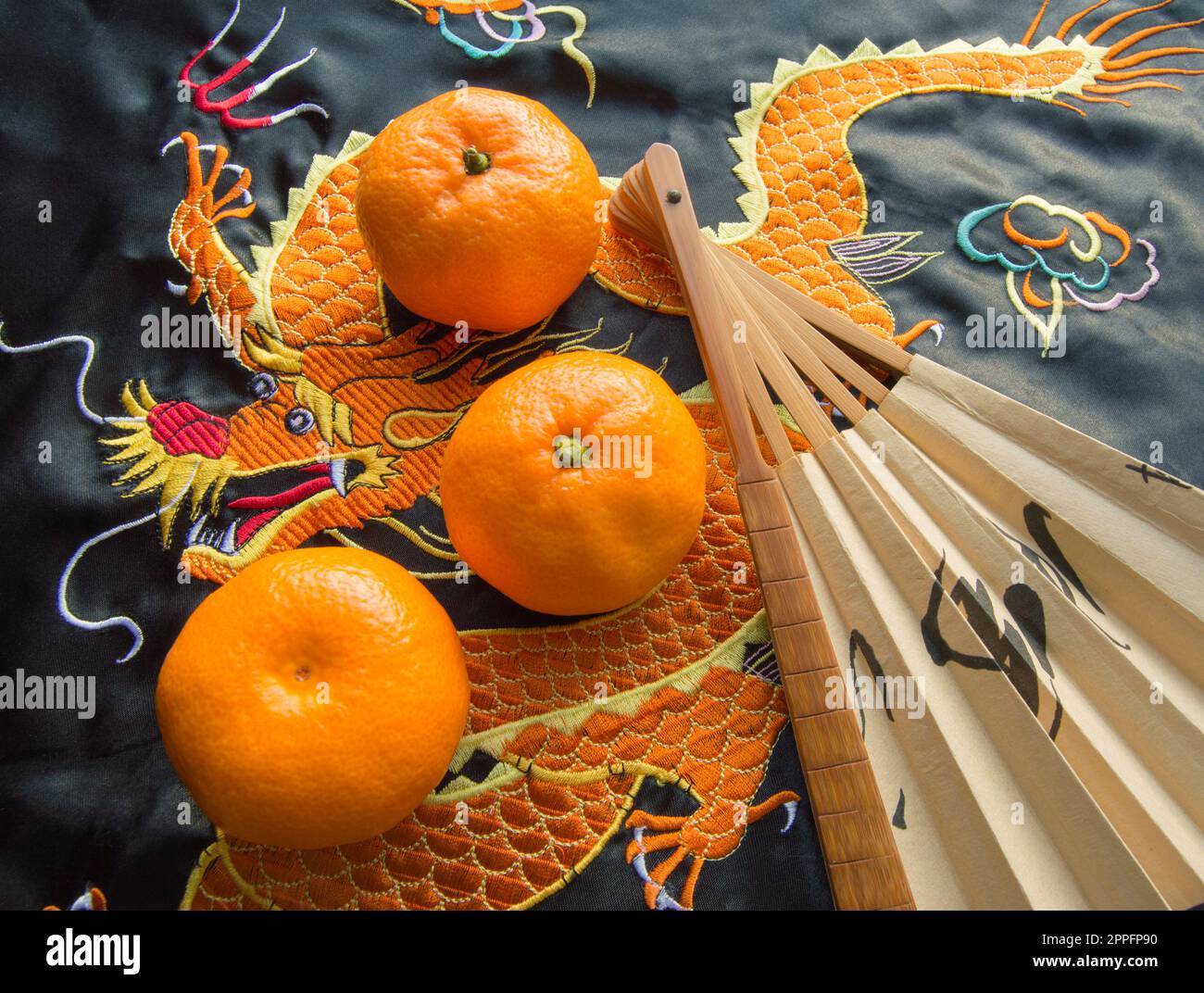 Chinesisches Neujahr, Mandarinen und ein Fan, der auf dem Seidenstoff mit einem bestickten Drachen liegt Stockfoto