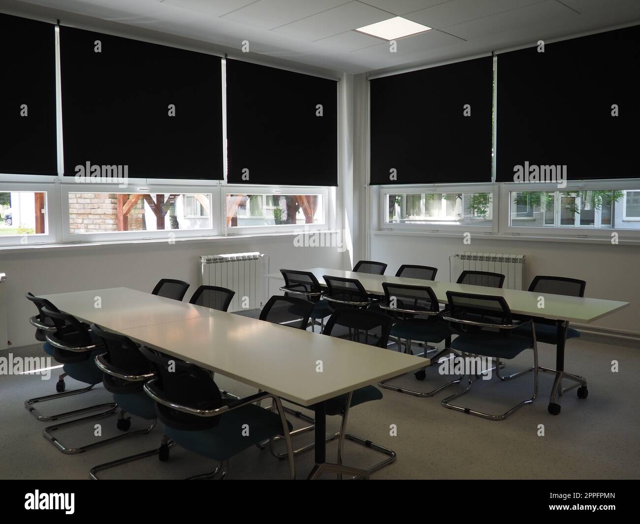 Tisch und Stühle im Besprechungsraum im Büro, im Klassenzimmer oder im Bibliothekssaal. Weiße, schwarze und graue Farben im Innenraum. Schwarze Jalousien zum Verdunkeln des Raums. Modernes Innendesign Stockfoto
