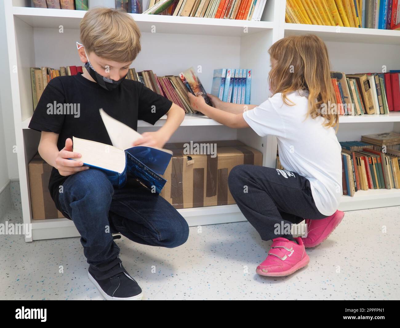 Sremska Mitrovica, Serbien, 15. Mai 2021 Kinder in der Schulbibliothek. Ein Junge und ein Mädchen suchen und blättern durch Bücher am Bücherregal. Der Junge liest ein sehr dickes Buch. Schulbildung. Teenager lernen Stockfoto