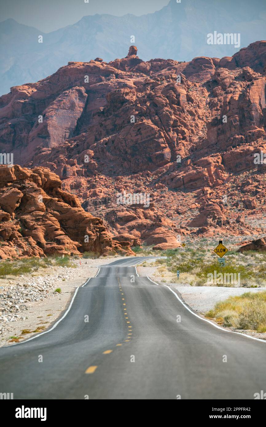 Gerade Straße im Valley of Fire und rötliche Felsen im backgrnd Stockfoto