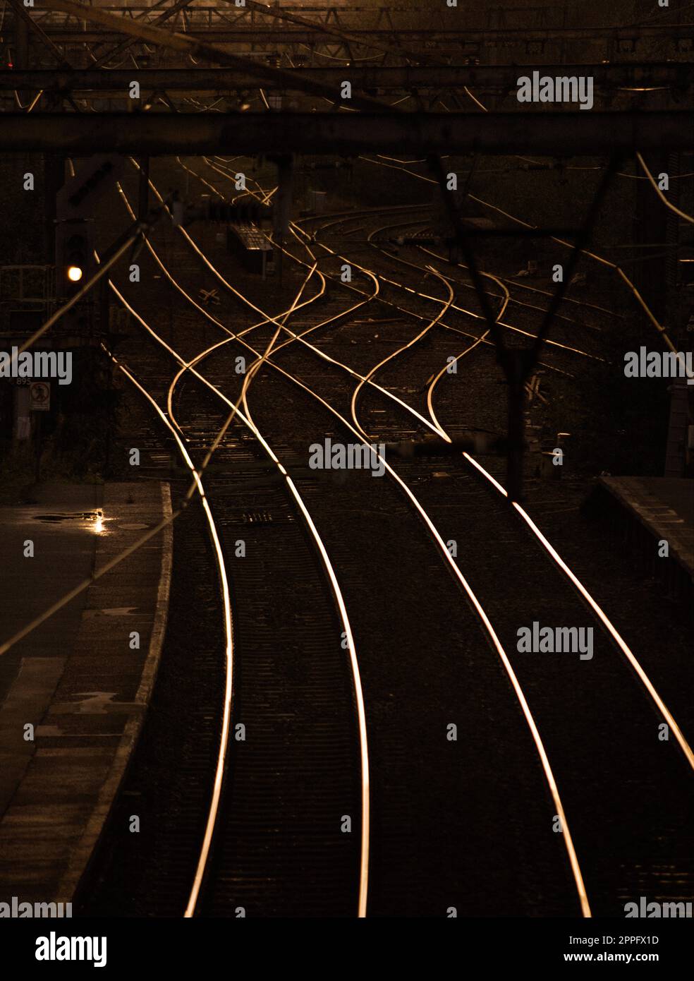 Zuggleise reflektieren das Abendlicht nach Sonnenuntergang. Bahnlinien kreuzen sich in der Nähe eines Bahnhofs in Großraum Manchester und leuchten rot und orange. Stockfoto