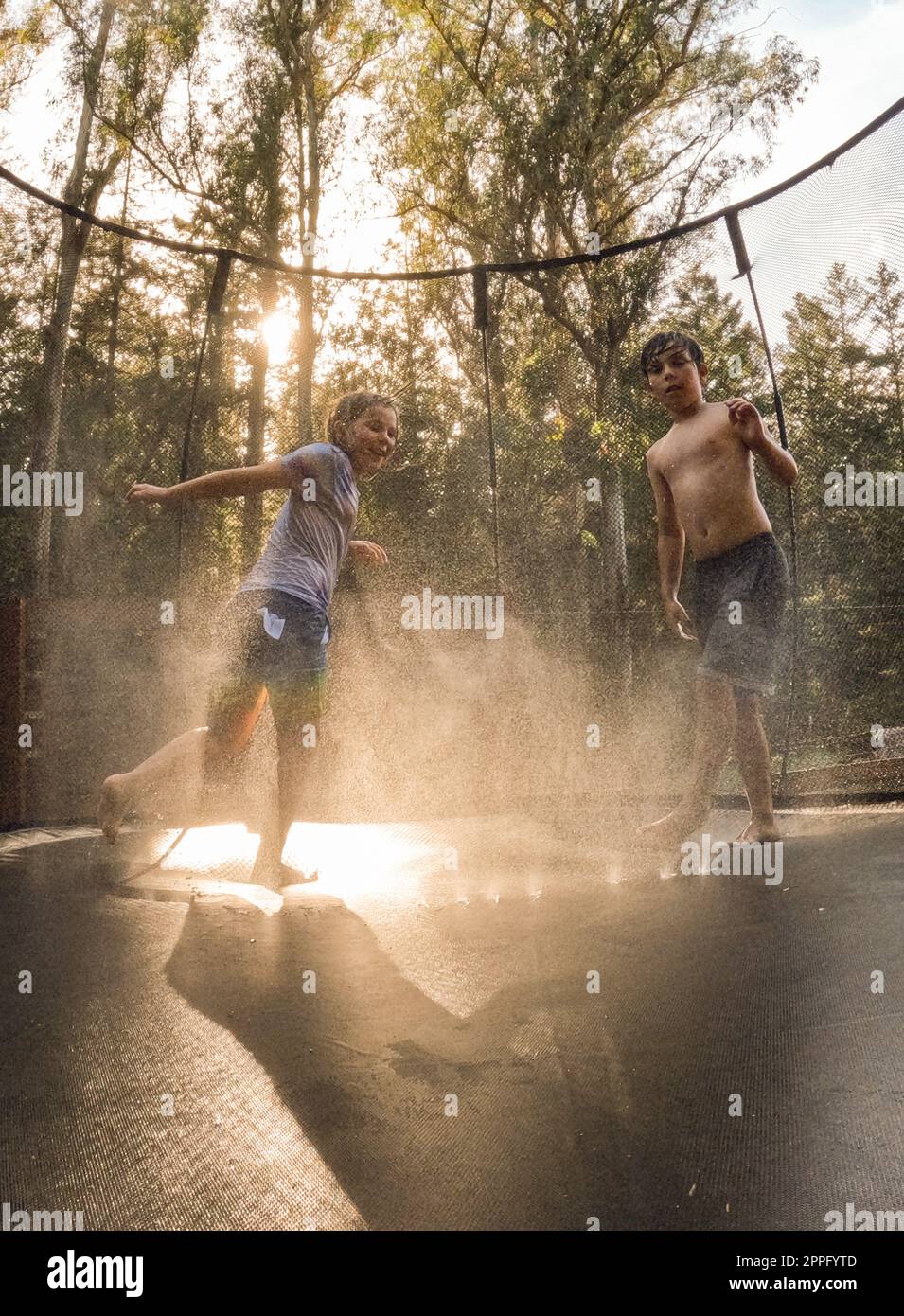 Geschwister bei Sonnenuntergang auf Trampolin mit Sprinklerwasser Stockfoto