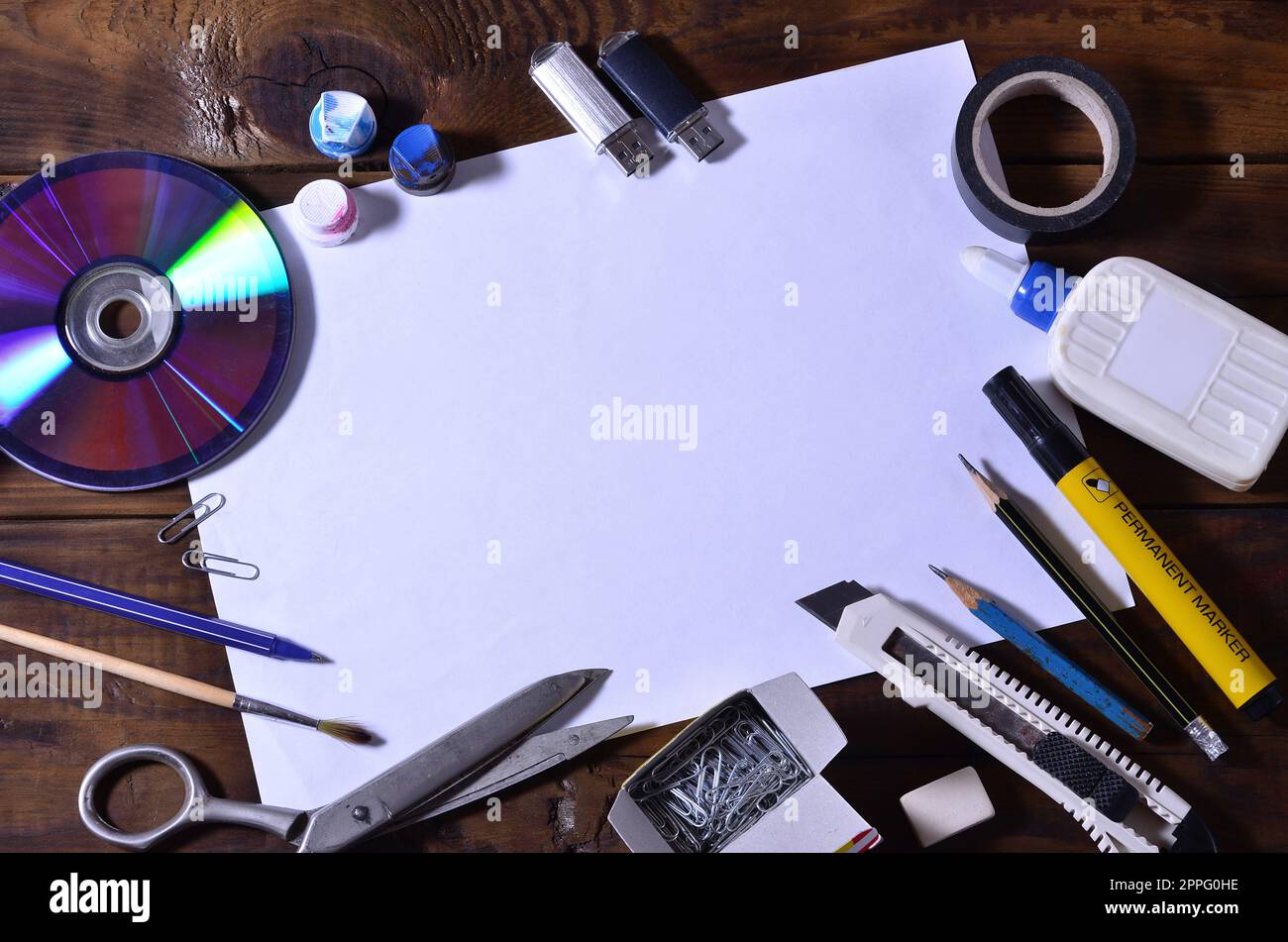 Eine Schule oder Büro Stillleben mit einem weißen leeren Blatt Papier und viele Büromaterialien. Das Schulmaterial liegt auf einem braunen Holzhintergrund. Für Text platzieren Stockfoto